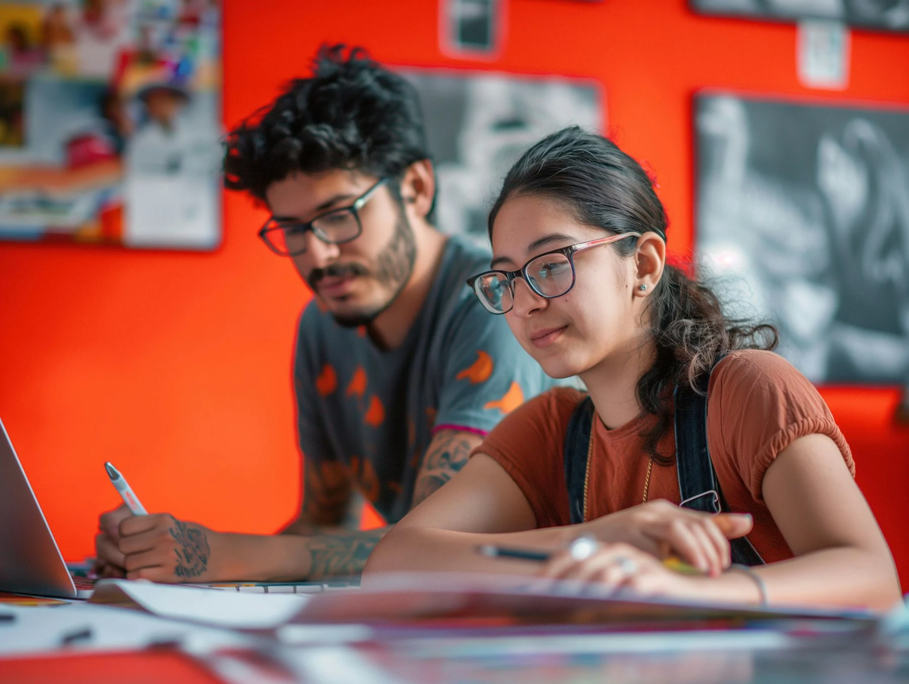 Duas pessoas trabalhando em uma mesa diante de um fundo vermelho